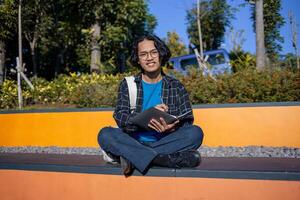 A male student is sitting in the park and writing on a book. photo