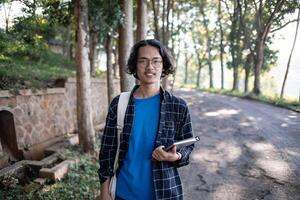 A male student wearing a shirt and glasses in the park is holding a book. photo