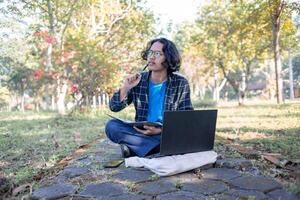 A male student is sitting with a laptop in the campus garden. With a thoughtful expression. photo