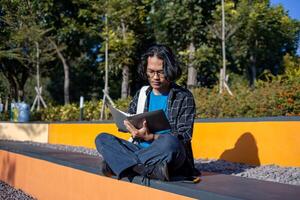A male student is sitting in the park and reading a book. photo