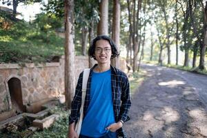 A man wearing a plaid shirt stands in the park casually. photo