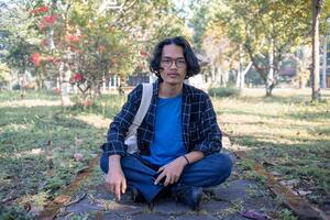 A man wearing a plaid shirt sits in the park relaxed and happy. photo