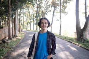 A man wearing a plaid shirt stands in the park casually. photo