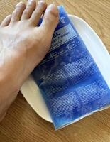 A foot rests on a blue gel ice pack placed on a white plate. The ice pack, used to reduce pain and swelling after a gout attack, shows condensation from being recently removed from the freezer. photo