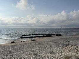 Remains of a shipwreck scattered on a sandy beach under a cloudy sky, with waves gently washing ashore. photo