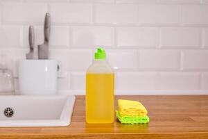 White plates, glass cups and forks in a clean white sink and two bottles of detergent and rags photo