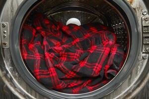 Red And Black Plaid Shirt Inside Open Washing Machine, Laundry Day Chores And Housekeeping Concept photo