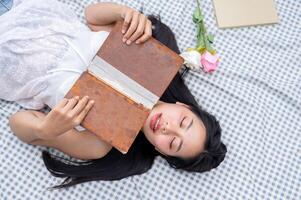 A top view of a positive, lovely Asian woman reading a book and lying on a picnic blanket. photo