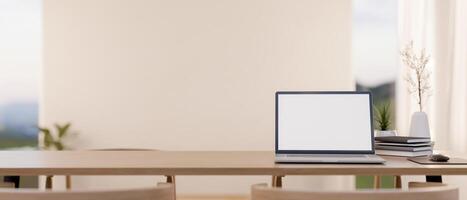 A wooden table featuring a laptop with a white screen mockup and decor, set in a bright room. photo