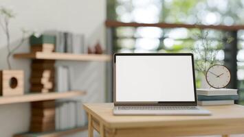 A close-up image of a laptop with a white-screen mockup on a wooden table in a room at home. photo