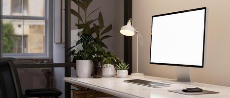 A computer mockup, a table lamp, and decorative plants on a table in a modern office room. photo