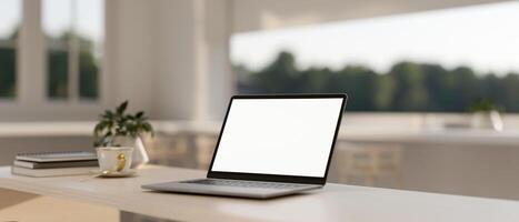 A laptop computer with a white-screen mockup on a table in a minimalist white room. photo