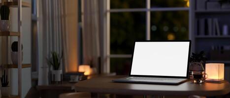 A laptop computer on a table in a room at home at night, illuminated by a table lamp. photo