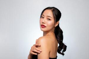A gorgeous Asian model touches her glowing tanned skin while posing against a grey studio background photo
