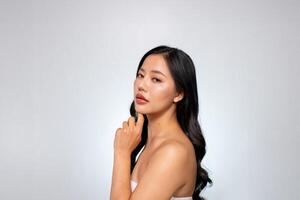 Elegant Asian woman poses against a grey background, looking at the camera while touching her chin. photo