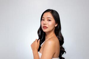 Gorgeous Asian woman poses against a grey background, showing her shoulder and looking at the camera photo