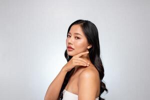 Elegant Asian woman poses against a grey background, looking at the camera while touching her chin. photo