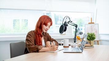 A charming Asian female radio host is working in her studio, focusing on adjusting the script. photo