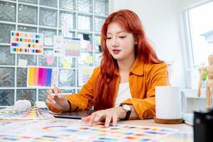 Beautiful Asian female designer is working in her studio, using a digital tablet and color swatches. photo