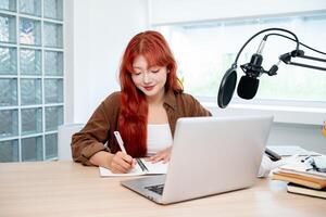 A charming Asian female radio host is working in her studio, focusing on adjusting the script. photo