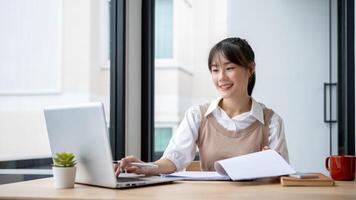 An Asian businesswoman is working at her desk, reviewing business report and working on her laptop. photo