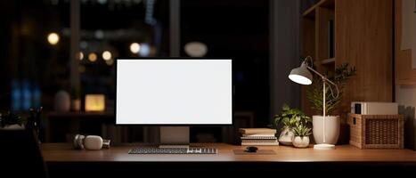 A modern dark office at night, a computer mockup on a desk, illuminated by a table lamp. photo