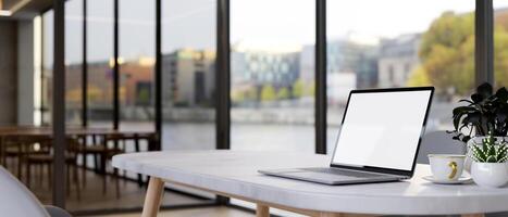 A laptop on a table by the window with a city view, in a contemporary office co-working space. photo