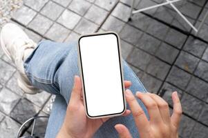 Top view image of a woman in jeans sitting outdoors, using her smartphone, touching on the screen. photo