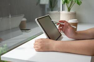 A close-up image of a woman writing on a digital tablet, working remotely from a coffee shop. photo