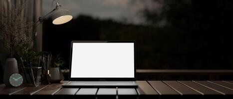 A laptop on a desk in a dark room at night, illuminated by a table lamp. photo