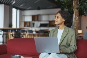 A woman in formal wear sits on a couch using a laptop computer for work in nice modern coworking office photo