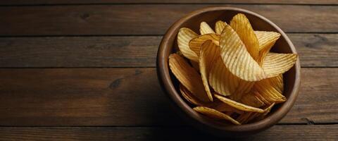 Corrugated golden potato chips in a wooden bowl on rustic wooden table Top view with Empty space for text , soft light, close up, macro. photo