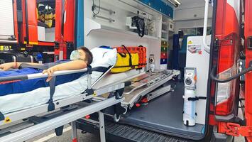 A teenage boy lies on a gurney in an ambulance, to provide first aid. Saving the life of a small ambulance patient. photo