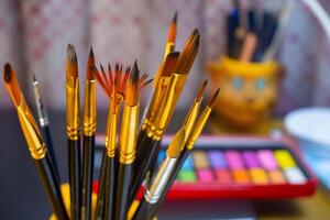 A set of painting brushes with a watercolor color palette background. Artistic equipment, paint brushes, watercolor color palette on work table photo