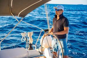 Young man captain stands at the helm and controls a sailboat during a journey by sea. High quality photo