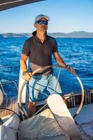 Young man captain stands at the helm and controls a sailboat during a journey by sea. High quality photo
