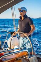 Young man captain stands at the helm and controls a sailboat during a journey by sea. High quality photo
