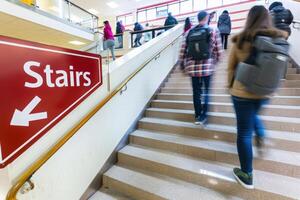A crowded stairwell filled with people ascending while a prominent sign directs towards the stairs, creating a dynamic atmosphere. photo