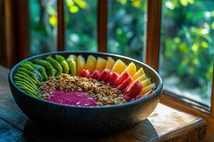 A delicious, colorful arrangement of fresh fruit and granola awaits on a rustic table, illuminated by warm sunlight filtering through the window. photo