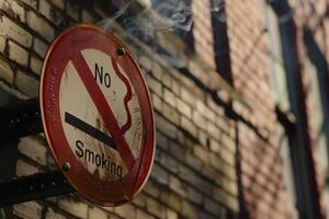 A close-up view of a No Smoking sign, its surface marked by age, hangs against a textured brick wall, emphasizing a clear message in a public space. photo