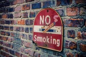 The sign, aged and slightly worn, firmly states a smoke-free message, showcasing rust and the texture of the brick behind it. photo