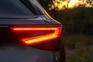 A striking tail light glows brightly, reflecting the graceful lines of a luxury vehicle against a dusky backdrop. photo