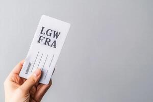 A hand grips an airline ticket, signaling the excitement of travel, with a minimalistic gray backdrop enhancing the focus on the travel document. photo