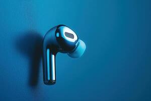 A stylish wireless earbud floats effortlessly, reflecting light in a captivating blue setting, embodying modern design and technology. photo