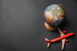 A vibrant red airplane sits alongside a detailed globe, symbolizing the spirit of adventure and global exploration against a sleek, solid background. photo