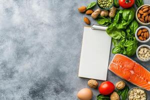 A well-organized display featuring fresh vegetables, nuts, fish, and a blank notepad for dietary planning, set against a clean solid background. photo