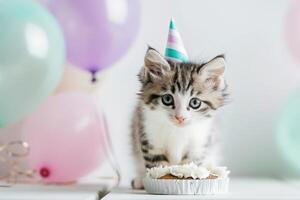 A playful kitten in a party hat eagerly approaches a small cake amid colorful balloons, creating a festive atmosphere. photo