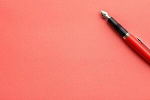 A sleek contact management list lies on a smooth coral surface, accompanied by a classic fountain pen poised for writing. photo