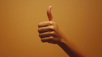 A Hand Giving a Thumbs Up Gesture Against a Brown Background photo