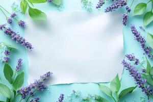 Lavender Flowers and Green Leaves Around a White Sheet of Paper on a Blue Background photo